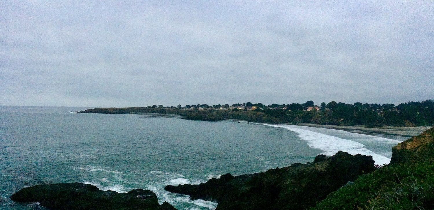 A scenic coastal view with rocky cliffs, ocean waves, and a cloudy sky in the background.