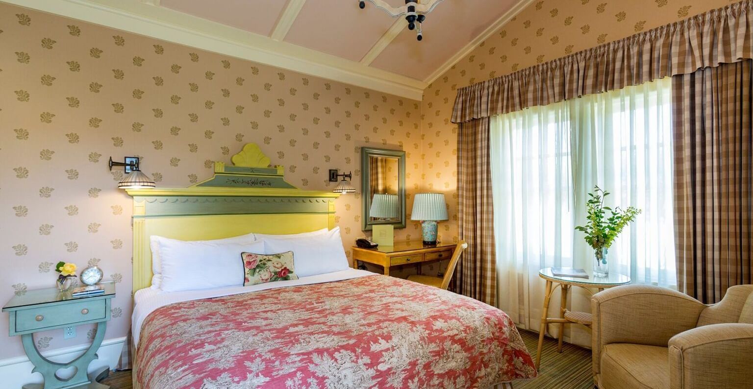 A charming and comfortable guest room at the Tallman Hotel, with a sloped ceiling, a double bed, and elegant decor.