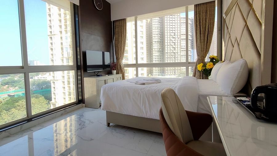 deluxe room at Maxxvalue Hotel, Chitranjan Tower, Powai with a posh bed and white linens along with floor-to-ceiling windows offering ciy view2