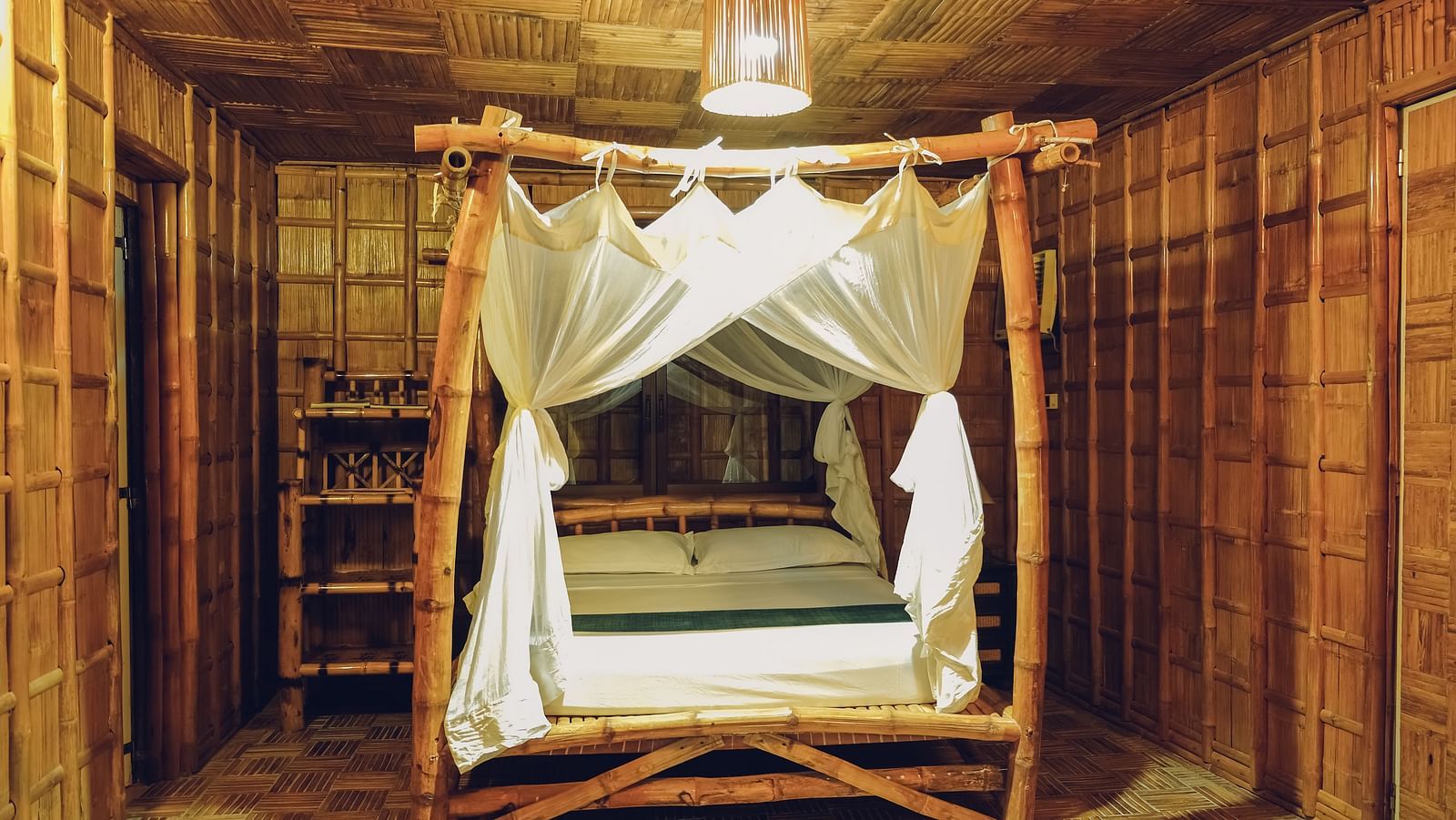 Standard Bamboo Suite at Flower Island Resort featuring a wooden canopy double bed,  bright lighting, and bamboo flooring.