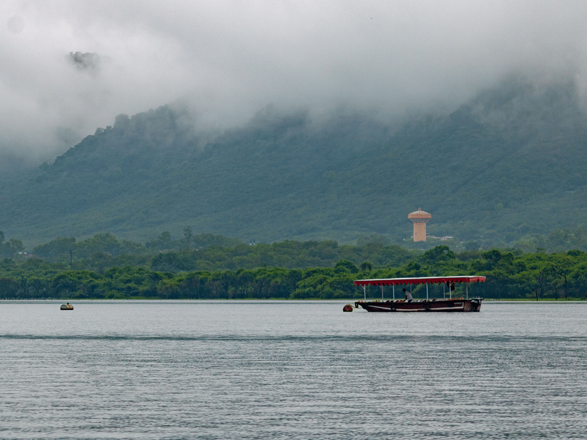 Boat sailing on Fateh Sagar Lake with misty hills calm waters and soft clouds drifting over tranquil Udaipur