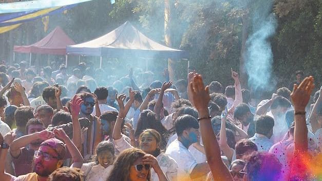 Crowd raising hands and cheering as Holi colours fill the air at the festival.