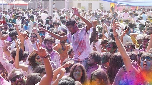 People dancing under colourful decorations, covered in Holi powders, celebrating with energy and enthusiasm.