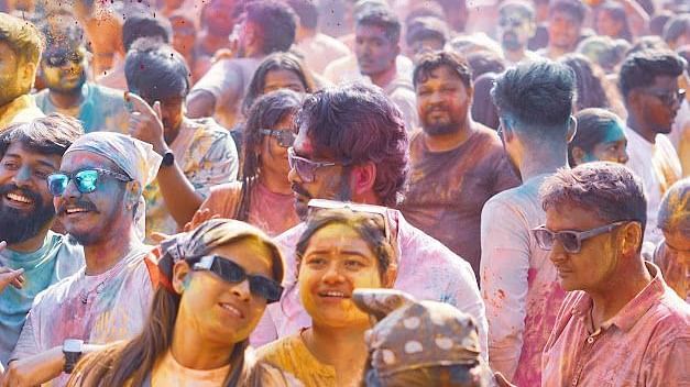 Two men posing happily at Holi festival, wearing sunglasses and covered in colourful powder.