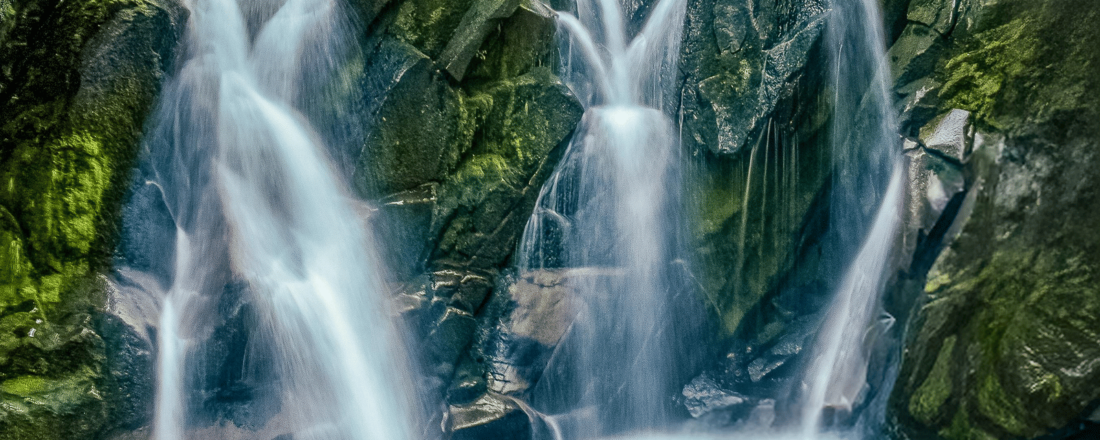 A waterfall cascading down rocky cliffs covered with moss and green vegetation into a pool below.
