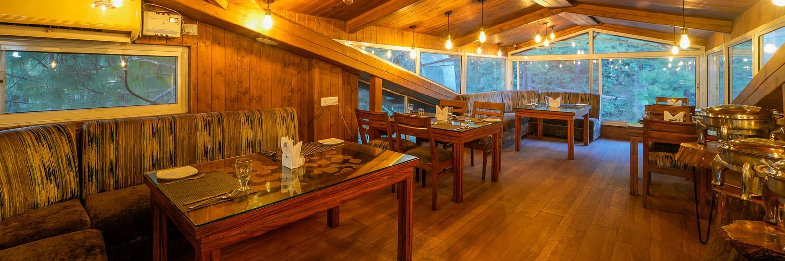The wooden interior of Ruttba at DLS Whispering Winds with chairs and tables with a view from the glass windows