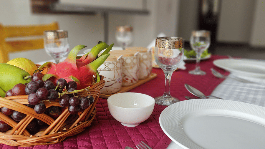 A close-up of a dinner table set with a red runner, white plates, and a basket of fresh fruit at Indus Serenity Retreat.