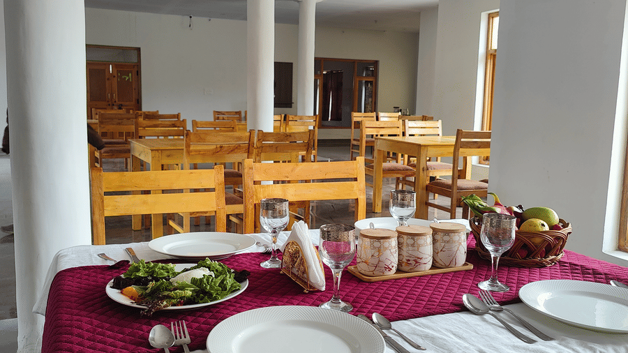 A perspective view of a set dining table with wooden chairs in a bright, open-plan restaurant at Indus Serenity Retreat.