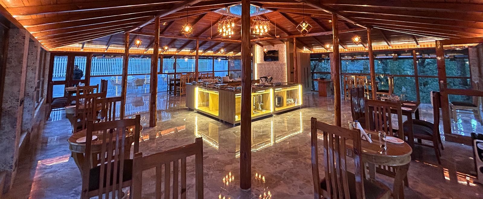 An image of the restaurant at DLS The Emerald, Nainital with wooden interiors along with chairs and tables and the area is lit with bright lighting
