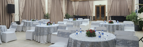 Elegant event hall with round tables covered in patterned tablecloths, white chairs, floral centerpieces, and soft overhead lighting - Suryavilas Luxury Resort and Spa