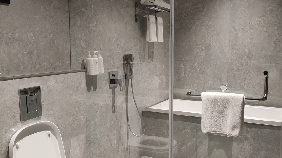 A bathroom at Anant Mahal, Jaipur featuring a glass walk in shower, a white toilet, and grey tiled walls with a chrome towel rack.