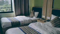 A hotel room featuring twin beds with plush linens and patterned runners next to a large window.