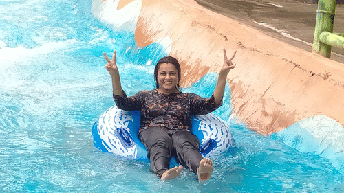 A woman enjoying a thrilling moment as she slides down a single man ride, smiling with excitement at Black Thunder, Coimbatore