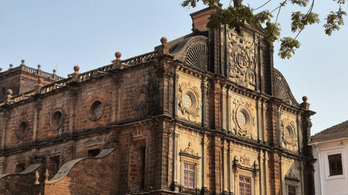 Historic stone building with arched windows and trees framing the facade.