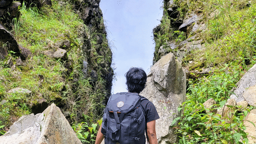 A lone hiker with a backpack walking through a narrow, grassy rocky ravine.