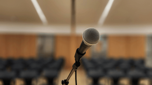 A close up shot of a microphone placed on a stage with seating arrangements in the background.