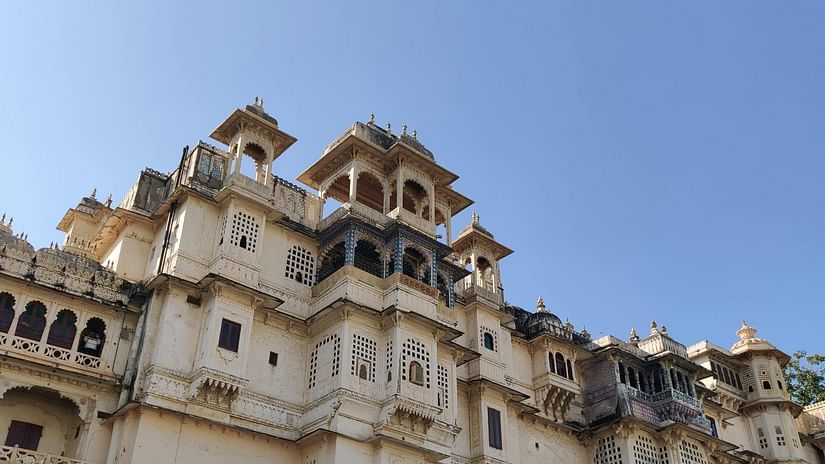 Low-angle shot of a palace, featuring its facade with multiple levels, balconies, and decorative elements under a clear blue sky.