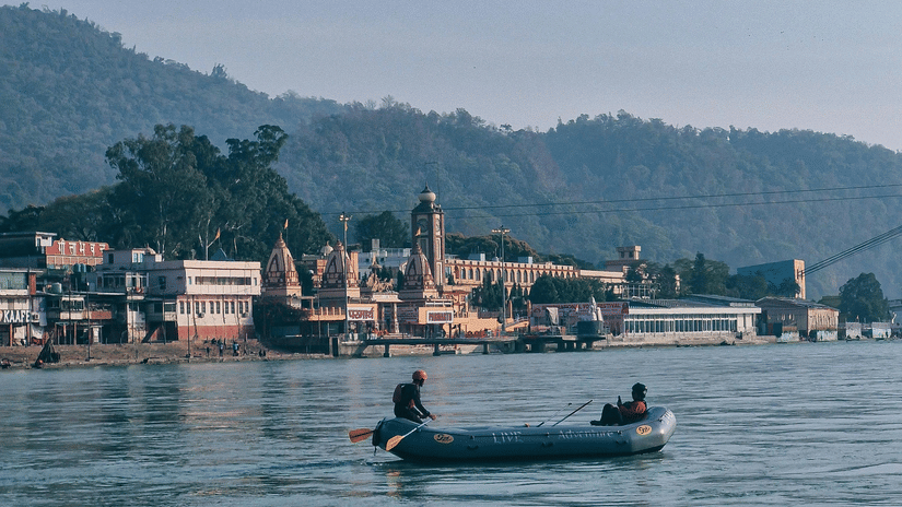 People on a boat, rafting on a calm river with mountains in the backdrop.