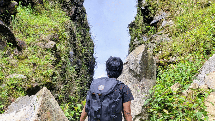A lone hiker with a backpack walking through a narrow, grassy rocky ravine.