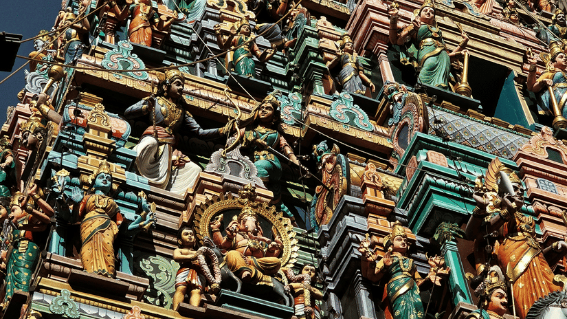 A view from below of a temple with numerous small idols on the gopuram in a layered architecture