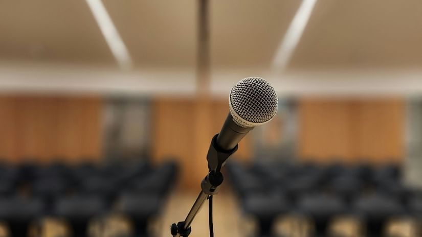 A close up shot of a microphone placed on a stage with seating arrangements in the background.