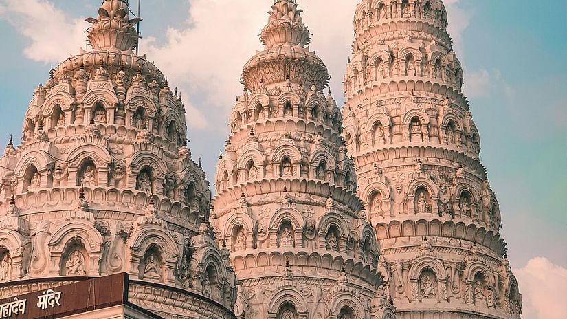Exterior view of the top portion of an Indian temple, featuring a hoisted flag and marvellous architecture.