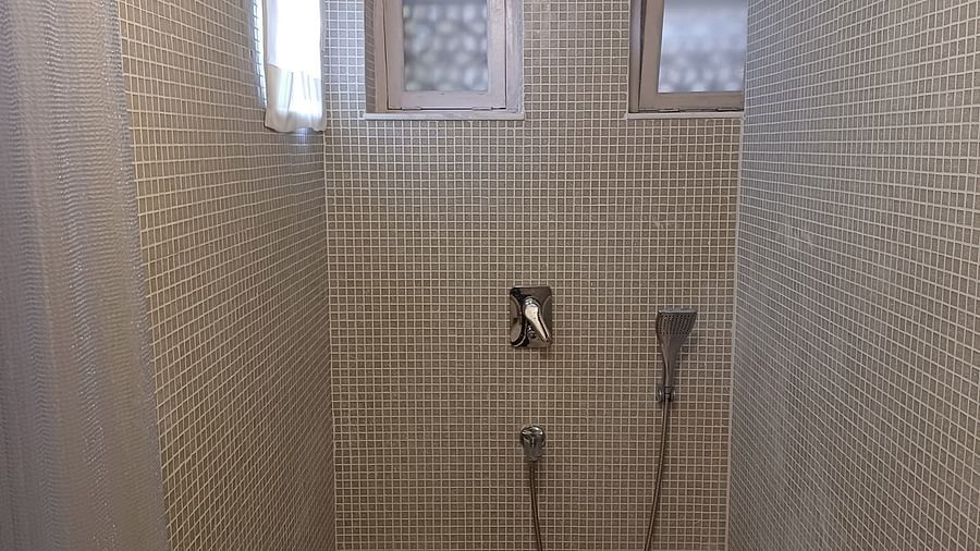 Walk-in shower with beige stone tiles, rainfall showerhead, and handheld spray at Neemrana Fort-Palace.