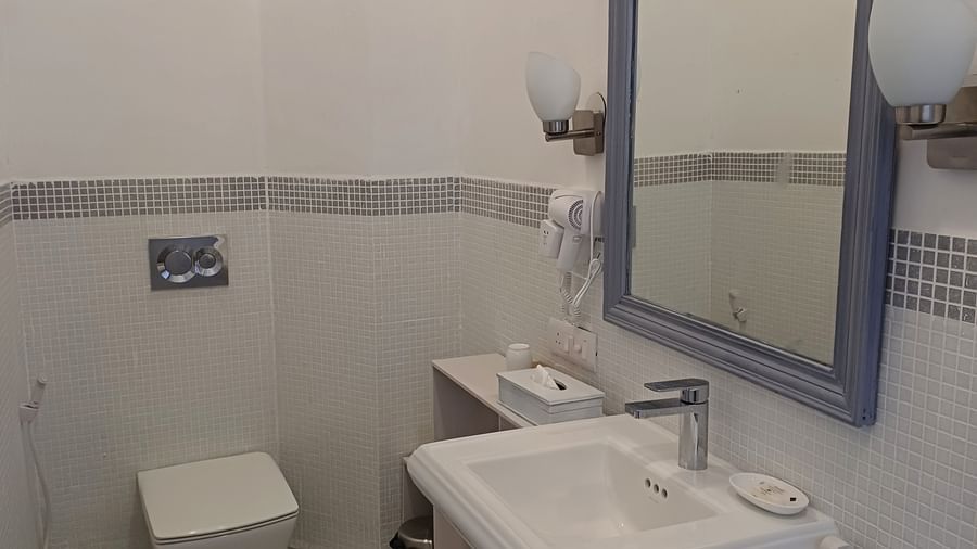 Compact bathroom with mosaic tile accents, wall-mounted toilet, pedestal sink, and modern fixtures at Neemrana Fort-Palace - 15th Century, Delhi-Jaipur Highway.