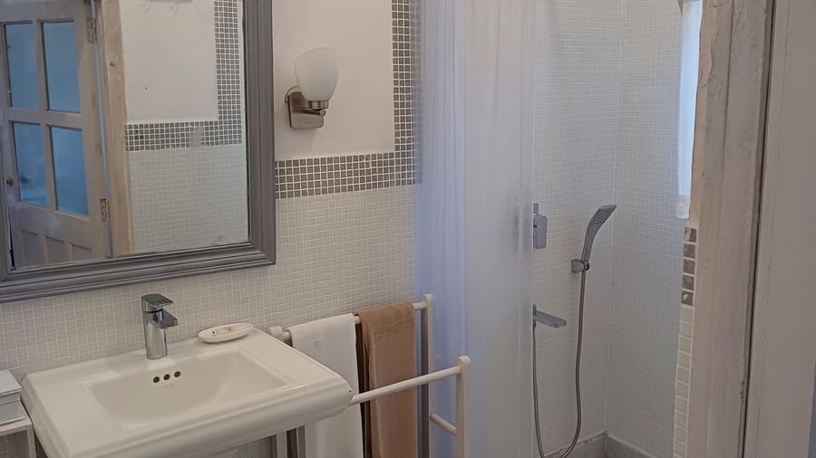 Clean bathroom with shower area, white curtain, pedestal sink, towel rack, and tiled walls at Neemrana Fort-Palace - 15th Century, Delhi-Jaipur Highway.