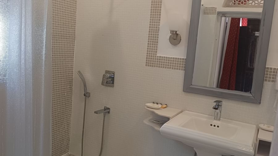 Modern bathroom with mosaic tile shower, rainfall showerhead, pedestal sink, and gray-framed mirror at Neemrana Fort-Palace - 15th Century, Delhi-Jaipur Highway.