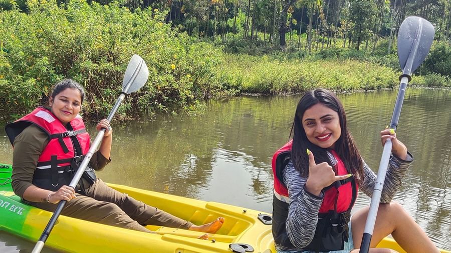 Two women in life jackets smiling while kayaking on a serene river with dense foliage in the background - Evergreen County
