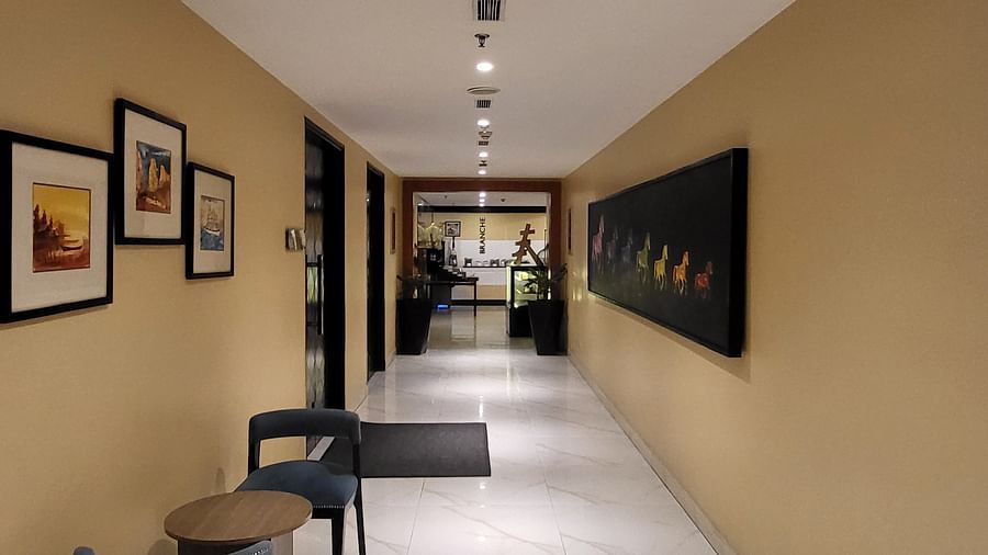 An image of a corridor at Golden Suites Gurgaon featuring seating small chairs and tables at one side, photo frames on the walls, and several doors leading to each room