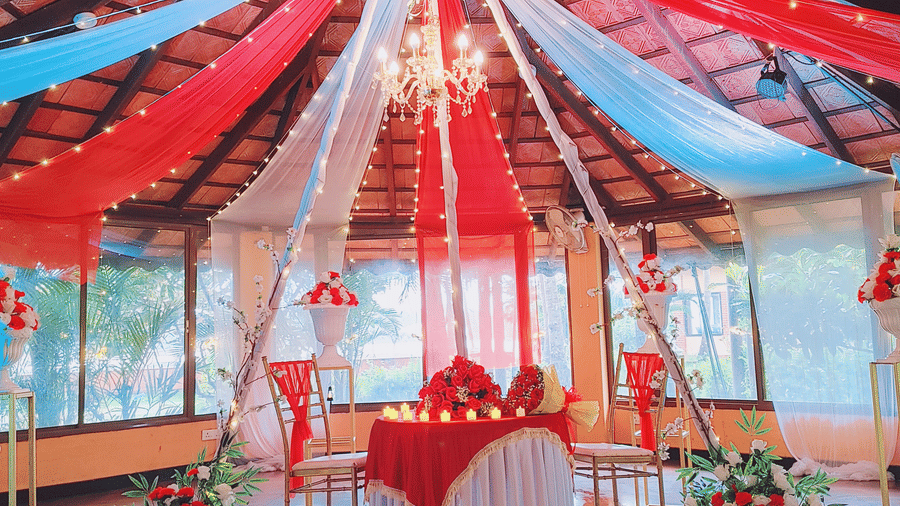'Will You Marry Me' proposal decoration in an indoor set up with red and white drapes and floral arrangements at Paradise Lagoon Resort, Udupi.