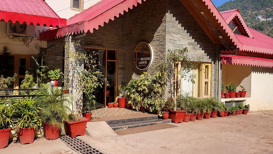 A frontal view featuring stone architecture, red rooftops, and lush surroundings at Dagshai Manor Kasauli - Inde Hotels.