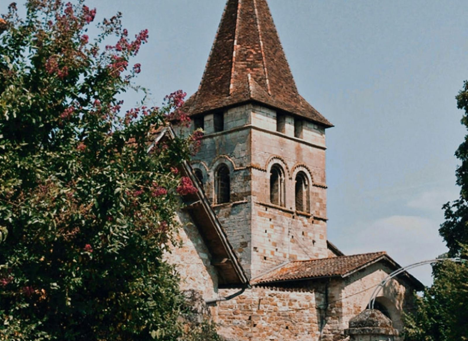 A partial view of an old stone church with a tall spire covered in red climbing plants.