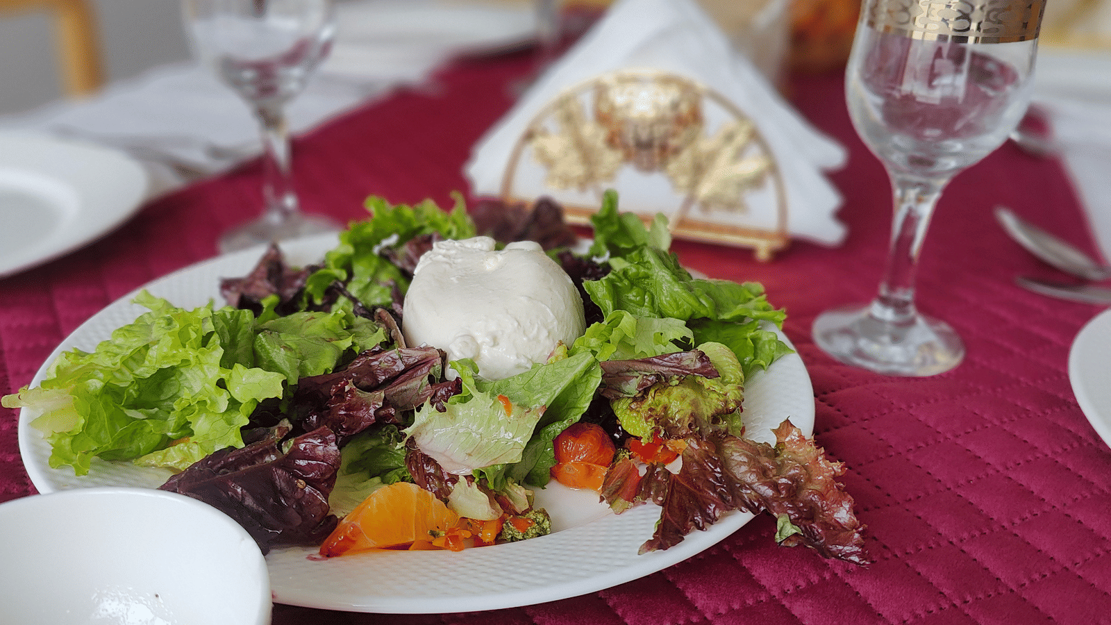 A close-up of a fresh green salad served on a white plate over a textured red table runner at Indus Serenity Retreat.
