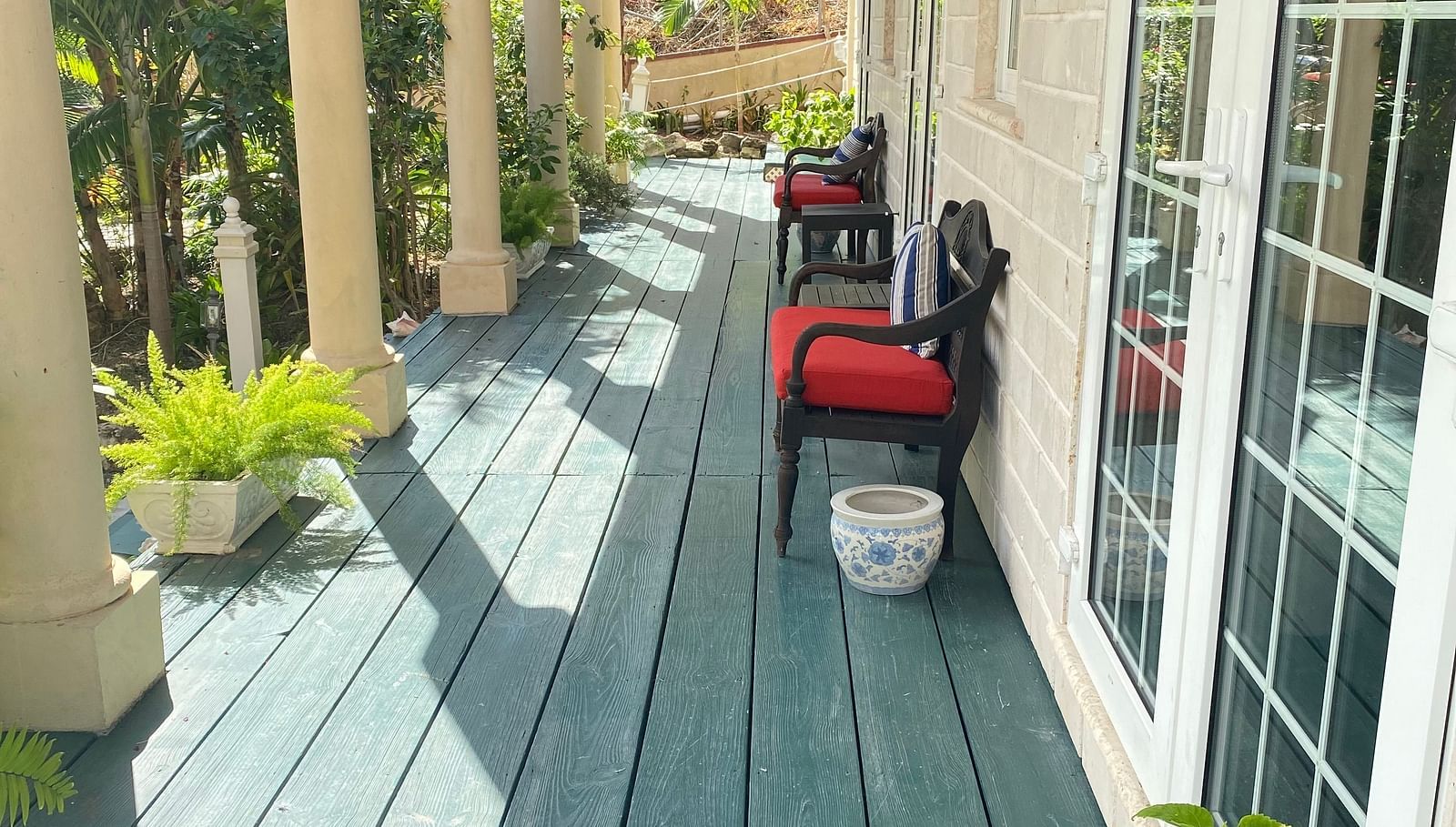Outdoor walkway with green wooden flooring and red chairs outside a room | A Stone's Throw Away