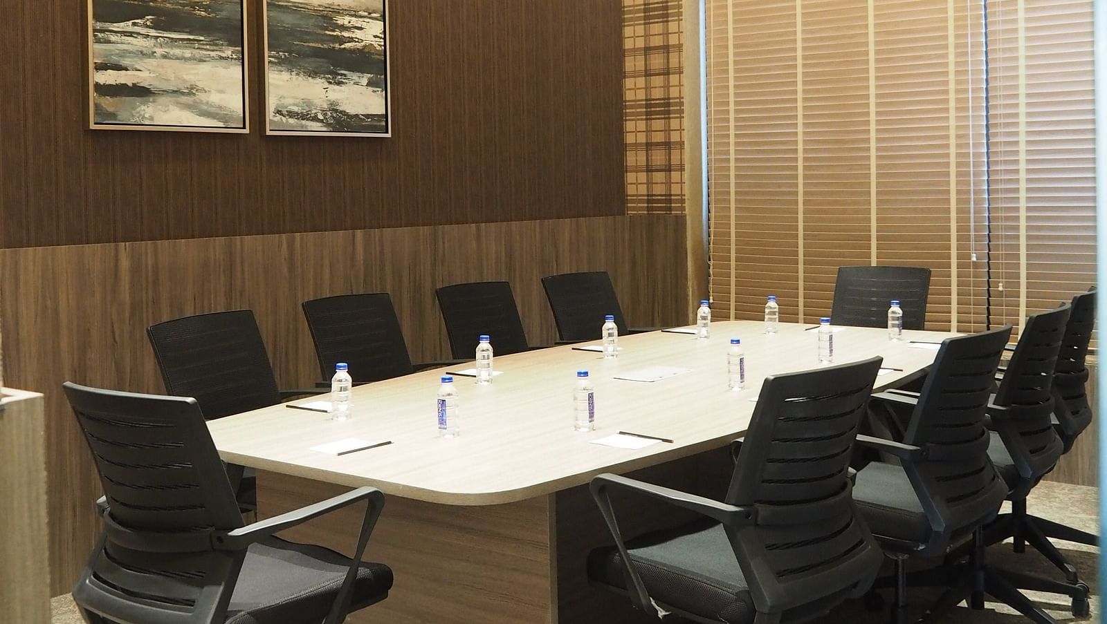 A meeting table with multiple chairs with a dark wall agianst it with a framed picture - Club Charholi, Pune 