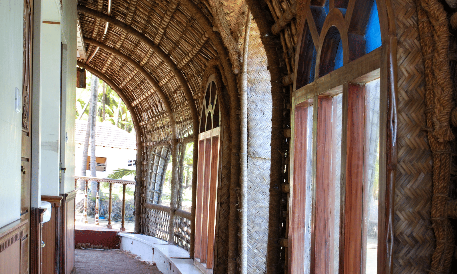 Curved corridor of house boat with arched brick walls, tiled flooring, and an open side with a railing at Paradise Lagoon Resort, Udupi.