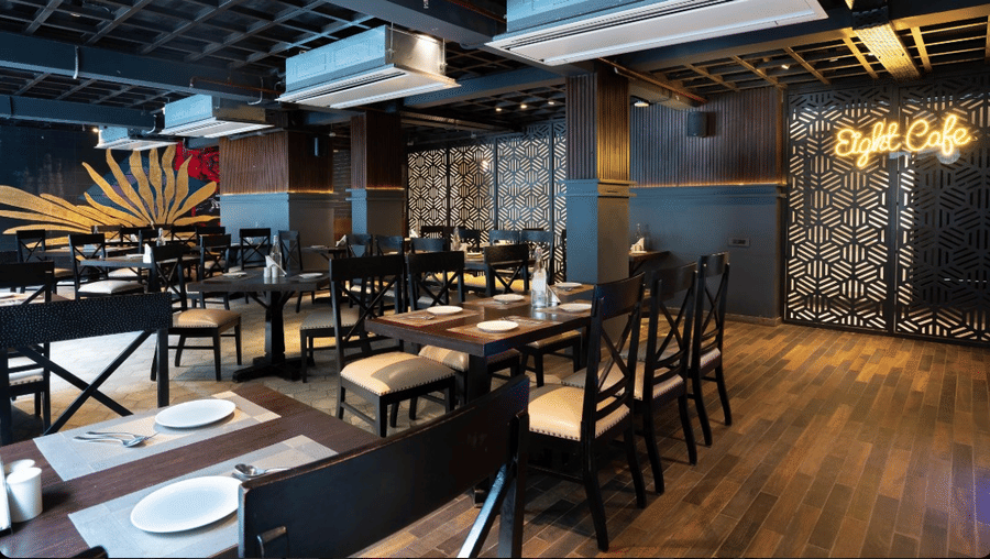 An indoor restaurant area featuring dark wooden tables and chairs under a black exposed ceiling with yellow lighting | Lawrence Solitaire Resort, Nainital