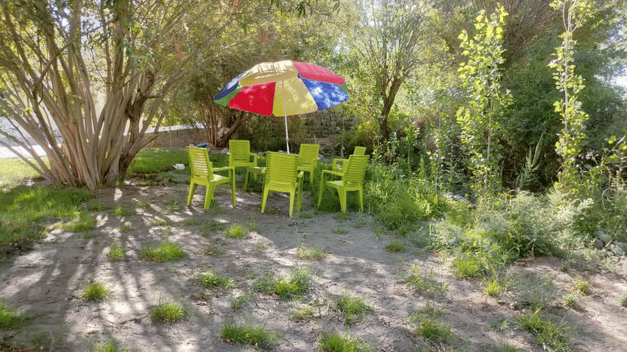 A shaded outdoor seating area with green chairs and a multi-coloured parasol set amongst trees at Indus Serenity Retreat.