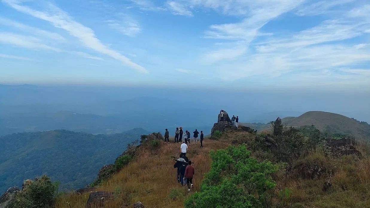 A group of trekkers walking along a scenic mountain ridge with expansive views of the valley below and a vibrant blue sky above.