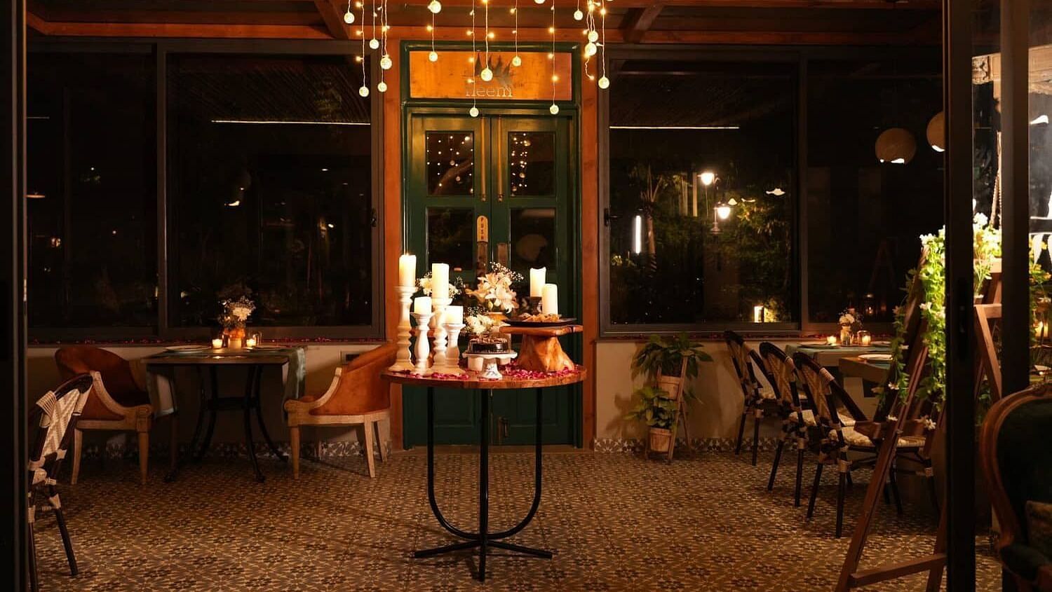 Indoor dining area at Karma Chalets with chandeliers, decorated tables, and large glass windows.