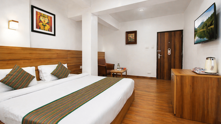An alternate angle view of a room at Central Hotels showing a king bed with blue and white bedding wooden wall panels hardwood flooring framed artwork and wall-mounted TV near the door.