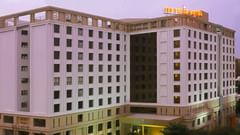 Facade of Pride Plaza Ahmedabad hotel with its name lit up atop the building, set against a glowing sunset sky for a striking evening view