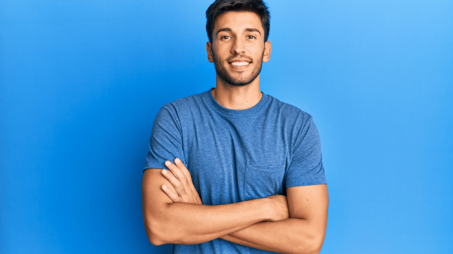 Man in a blue shirt standing against a blue background with arms crossed.