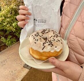 An image of a woman holidng doughnut which has chocolate sprinklers and is placed on a plate