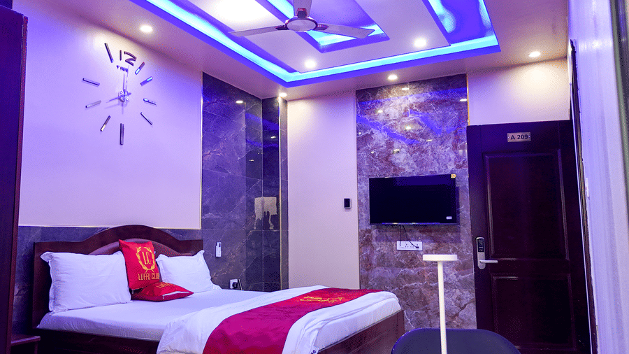 Hotel room showcasing a bed, wall clock, ceiling fan, and wall-mounted TV with purple and blue lighting - Luffu Club