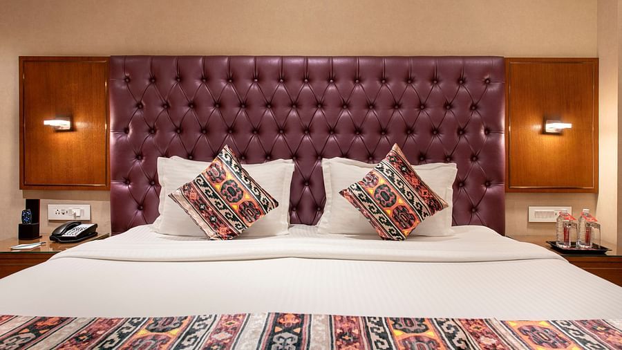 A close-up of a comfortable hotel bed featuring a plush purple headboard and decorative cushions with an ornate bed runner - SK Lords Inn Ahmedabad