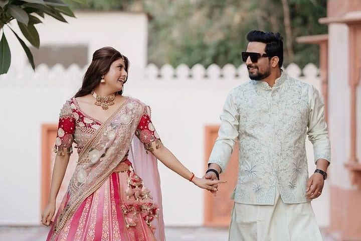 A couple walks hand in hand, smiling at each other, dressed in  traditional attire with intricate detailing. - Umaid Palace - A Lakeside Heritage Palace Resort